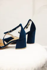 Zapato de tacón bajo color negro, con punta en V, tiras cruzadas en el empeine y cierre de hebilla en el tobillo. El tacón es ancho y mide 5 cm.