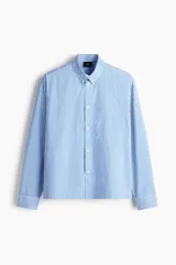 Camisa de corte relajado confeccionada en tejido de algodón con estampado de rayas verticales. Presenta cuello americano, cierre frontal con botones, un bolsillo en el pecho y mangas largas con puños abotonados.