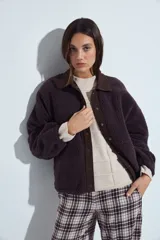 Campera de corderito color marrón oscuro, con cuello camisero y cartera frontal en tela lisa a tono. Presenta cierre mediante botones a presión y mangas largas con puños elásticos.