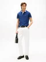 Chomba azul de algodón elástico con cuello y mangas ribeteadas en blanco. Tiene cartera de dos botones y logo de Tommy Hilfiger bordado en el pecho.