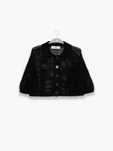 Camisa corta de punto abierto con cuello tipo polo, cierre frontal de botones y mangas tres cuartos. Presenta un diseño calado y un botón decorativo en forma de flor.