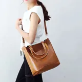 Bolso tipo tote amplio de cuero sintético color marrón, con asas cortas de mano y correa larga ajustable para llevar al hombro o cruzado.
