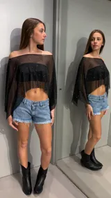 Capa corta de tul transparente color negro, con diseño off-shoulder, mangas amplias y aplicación de pequeños strass plateados distribuidos por toda la prenda.