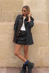 Falda mini de efecto engomado en color negro, con costuras a contratono en color marrón. Presenta diseño de cinco bolsillos, cierre frontal con botón y etiqueta de cuero con logo en la parte posterior.