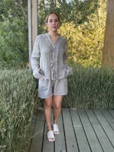 Camisa de lino color gris claro, de manga larga y corte holgado, con cuello mao y detalle de volados en el frente a lo largo de la botonera.