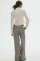 Pantalón sastrero de tiro alto con piernas amplias y pliegues frontales. Presenta un estampado de cuadros Príncipe de Gales en tonos grises, beige y negro.