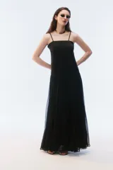 Vestido largo negro con breteles finos y escote recto, parte superior lisa y falda amplia de pliegues finos con gran movimiento y caída.