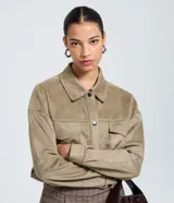 Camisa de corte regular confeccionada en gamuza sintética color beige, con cuello inglés, cierre frontal abotonado, mangas largas con puños ajustados y bolsillo tipo cargo en el pecho.