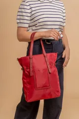 Bolso tipo tote bag de símil cuero color rosa pálido, con asas dobles y detalles de costura en color beige claro. Presenta un bolsillo frontal rectangular aplicado y herrajes metálicos.