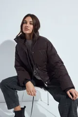Campera puffer de nylon color marrón oscuro, con cuello alto, cierre frontal y puños elásticos. Diseño acolchado de volumen ligero.