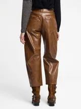 Pantalón de silueta globo confeccionado en cuero sintético con acabado efecto vintage. Presenta un corte de pierna ancha, cintura con cierre y botón, y costuras horizontales a la altura de la rodilla.