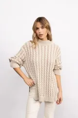 Sweater de punto con diseño de trenzas verticales, cuello alto y silueta oversize. Presenta aberturas laterales en el ruedo y mangas largas con puños acanalados.