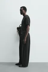 Pantalón chino de corte wide fit confeccionado en tejido de algodón. Presenta pliegues frontales, bolsillos laterales y bolsillos traseros de vivo, con cierre frontal de cremallera y botón.