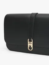Cartera de hombro negra con solapa frontal y correa ajustable. Presenta un broche metálico dorado con el monograma TH en el centro.