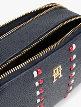 Cartera tipo bandolera Tommy Hilfiger de acabado granulado en color azul marino. Cuenta con dos compartimentos principales con cierre de cremallera, correa ajustable y detalles metálicos dorados. En el frente presenta el monograma TH metálico y una cinta decorativa vertical con los colores distintivos de la marca.