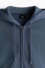 Campera con capucha de corte oversized, confeccionada en tejido de mezcla de algodón con interior suave. Presenta cierre frontal, hombros caídos, cordón ajustable en la capucha y bolsillos tipo canguro. Puños y bajo acanalados.