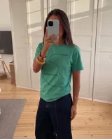 Remera de corte regular color verde, con cuello redondo y mangas cortas. Presenta un diseño gráfico estampado en el frente con flechas curvas y texto técnico.