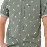 Camisa verde con estampado de palmeras blancas, de manga corta con dobladillo y corte clásico. Tiene cuello abotonado, bolsillo en el pecho y cierre frontal con botones.