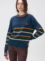 Sweater de punto cable con diseño a rayas horizontales en tonos marrón, amarillo y lila. Presenta cuello redondo acanalado, mangas largas con puños a juego y logo bordado en el pecho.