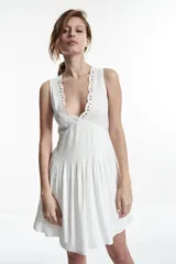 Vestido corto blanco con escote en V y detalle de puntilla en el escote.