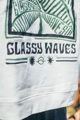 Hoodie de color natural con capucha y diseño bordado en la espalda que incluye motivos botánicos y la frase 'Glassy Waves'.