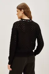 Sweater negro de punto calado con cuello polo decorado con apliques de piedras brillantes de colores. Presenta mangas largas con puños ajustados y un diseño elegante.