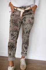 Pantalón de mujer con estampado animal print y detalles florales en tonos beige y negro, de corte recto y con ruedo doblado. Incluye un cinturón de tela beige y marrón.