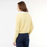 Chaqueta de punto con textura de croché en color amarillo pastel, con diseño de cuello en V, cierre frontal con lazada y terminaciones festoneadas en mangas y ruedo.