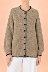 Cardigan de punto en color beige con textura tejida, cuello redondo y cierre frontal de botones. Presenta un detalle de borde festoneado en color negro en el cuello, la tapeta de botones, el ruedo y los puños.