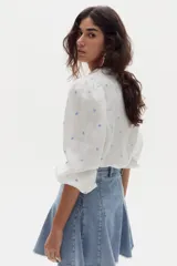 Camisa de lino blanca con bordados de pequeños corazones celestes, mangas abullonadas y cuello mao con volados en la botonera frontal oculta.