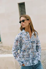 Camisa de manga larga con cuello solapa y cierre frontal de botones, confeccionada en tejido combinado semitransparente con estampado floral en tonos azules y blancos.