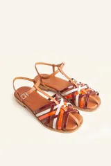 Sandalia plana de cuero blanco con diseño de tiras trenzadas en la parte delantera. Cuenta con una tira ajustable al tobillo con hebilla metálica y suela plana de color negro.