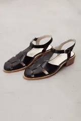 Sandalias tipo pescador de cuero negro con tiras entrelazadas, taco bajo cuadrado y tira ajustable con hebilla en el tobillo.