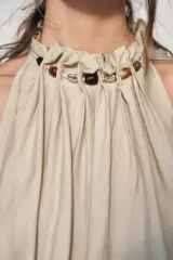 Top de cuello halter con diseño holgado y fruncido. Presenta detalle de abalorios decorativos en el escote y bajo con acabado elástico.
