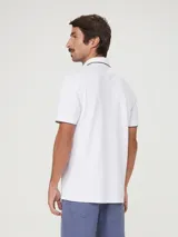 Remera polo blanca de manga corta, con cuello camisero y ribetes grises en cuello y puños. Cuenta con cierre frontal de botones y un pequeño logo bordado en el pecho.