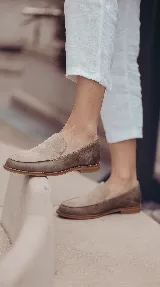 Mocasines de gamuza color tostado, con diseño clásico de pespuntes marcados en la parte delantera y suela plana.