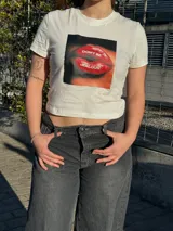 Top blanco de manga corta, corte crop top y ajuste ceñido al cuerpo. Cuenta con un estampado gráfico frontal cuadrado de unos labios rojos con la frase "Don't be jealous".