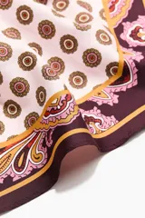 Pañuelo triangular de satén con diseño estampado en tonos bordó, rosado y marrón, combinando patrones paisley y geométricos.