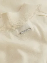 Sweater de lana merino color crema, de corte slim, cuello perkins y manga corta. Presenta detalles de puntadas en los hombros y ribetes de canalé en cuello, puños y bajo.