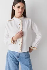 Camisa de lino blanca con detalles de volados tejidos a mano en crochet en cuello, cartera y puños. Presenta vivos a contratono en color marrón y cierre frontal con botones.