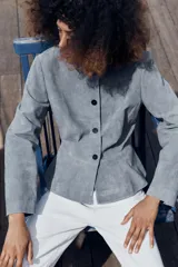 Chaqueta de cuero gamuzado color gris, con cuello redondo, manga larga, cierre frontal con botones oscuros y bajo con detalle peplum.