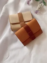 Billetera de cuero sintético con textura granulada, cierre de solapa con broche a presión y tira decorativa central.