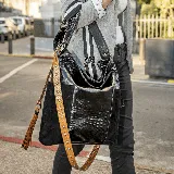 Bolso tipo tote de cuero vacuno negro con apliques de cuero con textura de cocodrilo y laterales de gamuza. Tiene correa de hombro ancha con rayas blancas y negras, correa bandolera desmontable con apliques de tachas y borla decorativa. Cuenta con cierre trasero, bolsillos laterales, forro interior, bolsillo interior con cierre y bolsillo para celular.