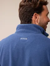 Campera de polar tipo sherpa en color azul, con cierre frontal completo, cuello alto y bolsillos laterales. Presenta un pequeño logo bordado en el pecho.