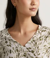 Blusa de crepé color blanco con estampado de hojas verdes, escote en V y mangas largas abullonadas con detalle de nudo en los puños.