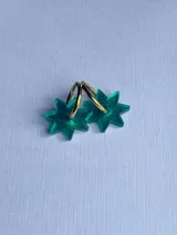 Aros tipo argolla con dije colgante en forma de estrella de ocho puntas, elaborado en acrílico traslúcido de color verde.