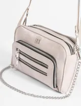 Bandolera negra de cuero vegano con correa ajustable y cadena lateral removible. Presenta un bolsillo frontal con doble cierre horizontal y un logo metálico cuadrado en la parte superior central.