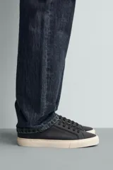 Zapatilla de estilo minimalista en color negro, con cordones al tono, suela de goma en color crema y detalle de talón en contraste.