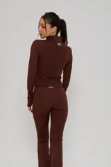 Conjunto deportivo de dos piezas color marrón, compuesto por una campera de cuello alto con cierre frontal y mangas largas con abertura para pulgar, y un pantalón de corte ajustado con terminación acampanada.