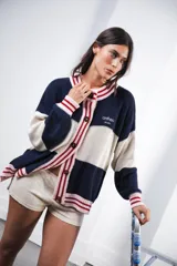 Cardigan oversized de punto grueso, color azul marino y blanco con franjas rojas y rosadas en el cuello, puños y solapa. Tiene botones grandes marrones y el logo de Anthea bordado en el pecho.